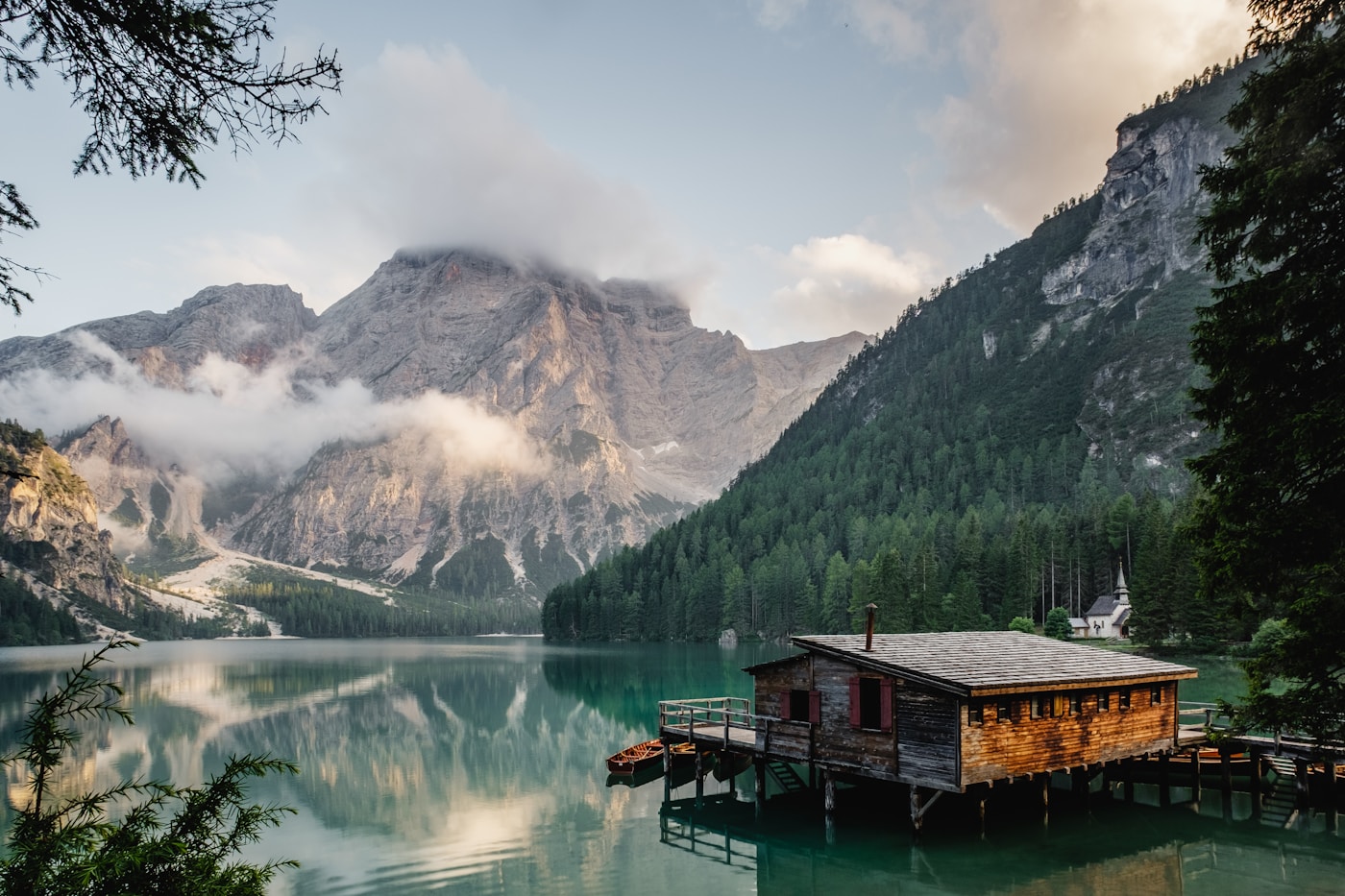 A small wooden cabin beside a still lake reflecting mountains and an evening sky